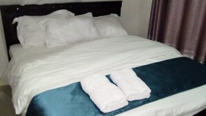 A neatly made bed with white linens and a blue accent, two folded white towels on the bed, and a dark headboard. - Apartment Sleeps 6 With Free Parking (Nairobi)