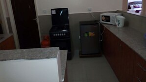 A compact kitchen with a gas stove, a refrigerator, a microwave, and a gas cylinder. - Apartment Sleeps 6 With Free Parking (Nairobi)