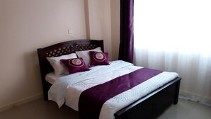 A neatly made bed with a dark headboard, white bedding, and two decorative pillows. - Apartment Sleeps 6 With Free Parking (Nairobi)