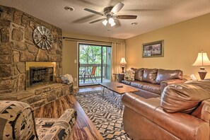 A living room with a stone fireplace, leather sofa, and a ceiling fan.