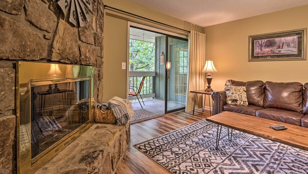 A living room with a stone fireplace, a brown leather sofa, a patterned rug, and a painting on the wall. - 1 Mi to Parkway! Flat-access Pigeon Forge Condo (Pigeon Forge)