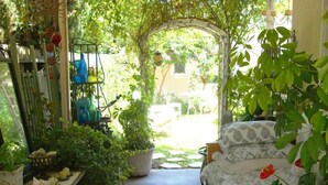 A cozy room with a bed, a table with plants, and a window overlooking a garden. - Charming Culver City Cottage w/ Shared Pool+garden (Culver City)