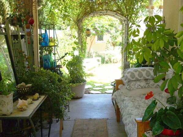 A cozy room with a bed, a table with plants, and a window overlooking a garden.