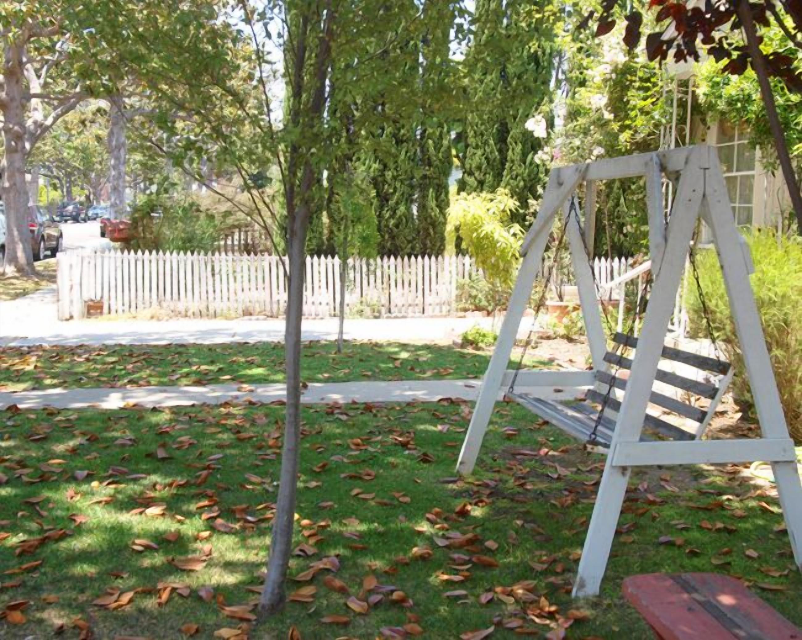 A wooden swing set in a grassy area with a white picket fence in the background.