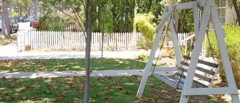 A wooden swing set in a grassy area with a white picket fence in the background.