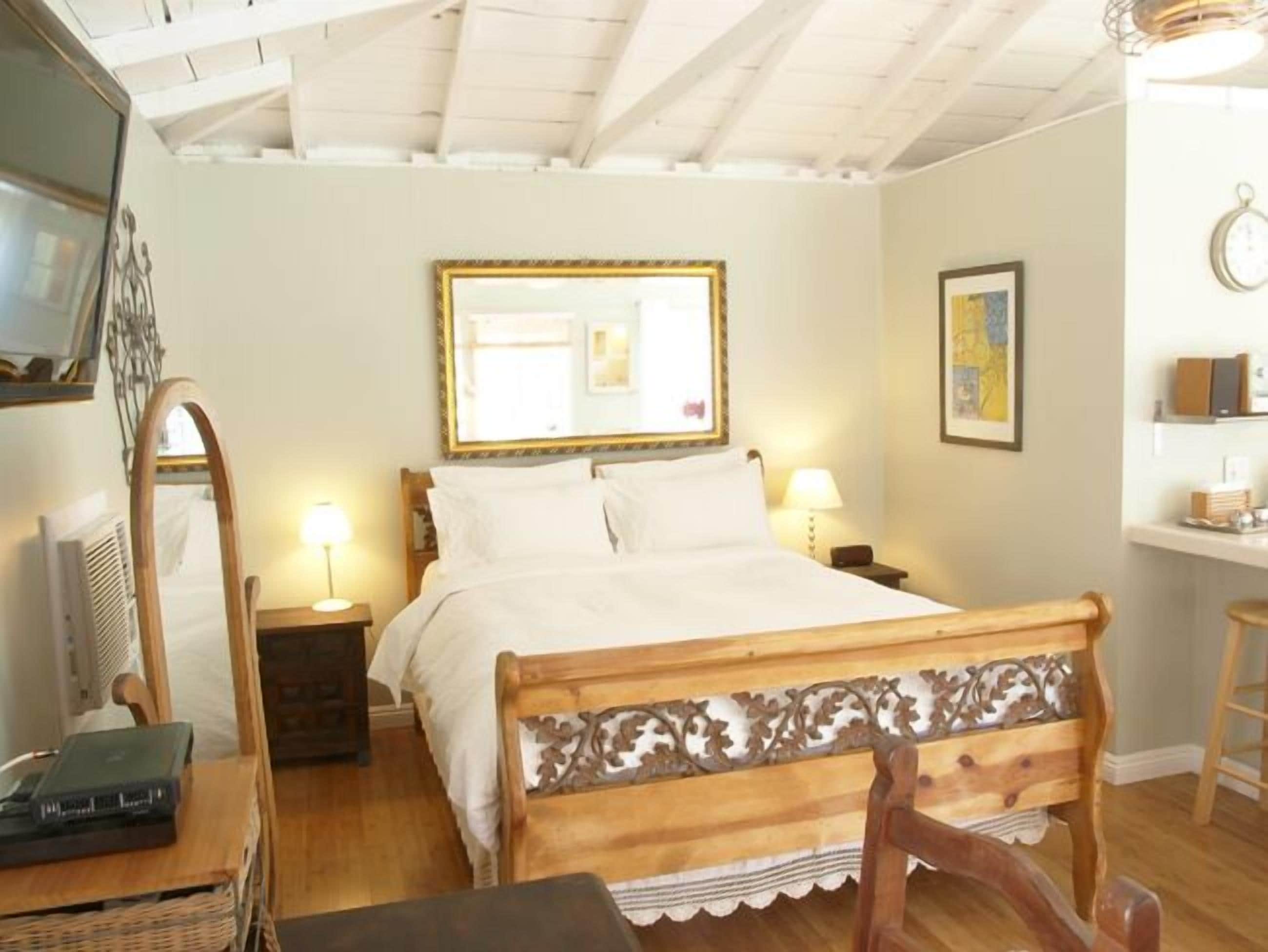 Ein Schlafzimmer mit einem hölzernen Bett, einem Spiegel, Nachttischlampen, einem kleinen Tisch und einem Stuhl.