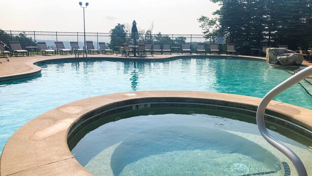 A swimming pool with clear water, a hot tub, and lounge chairs.