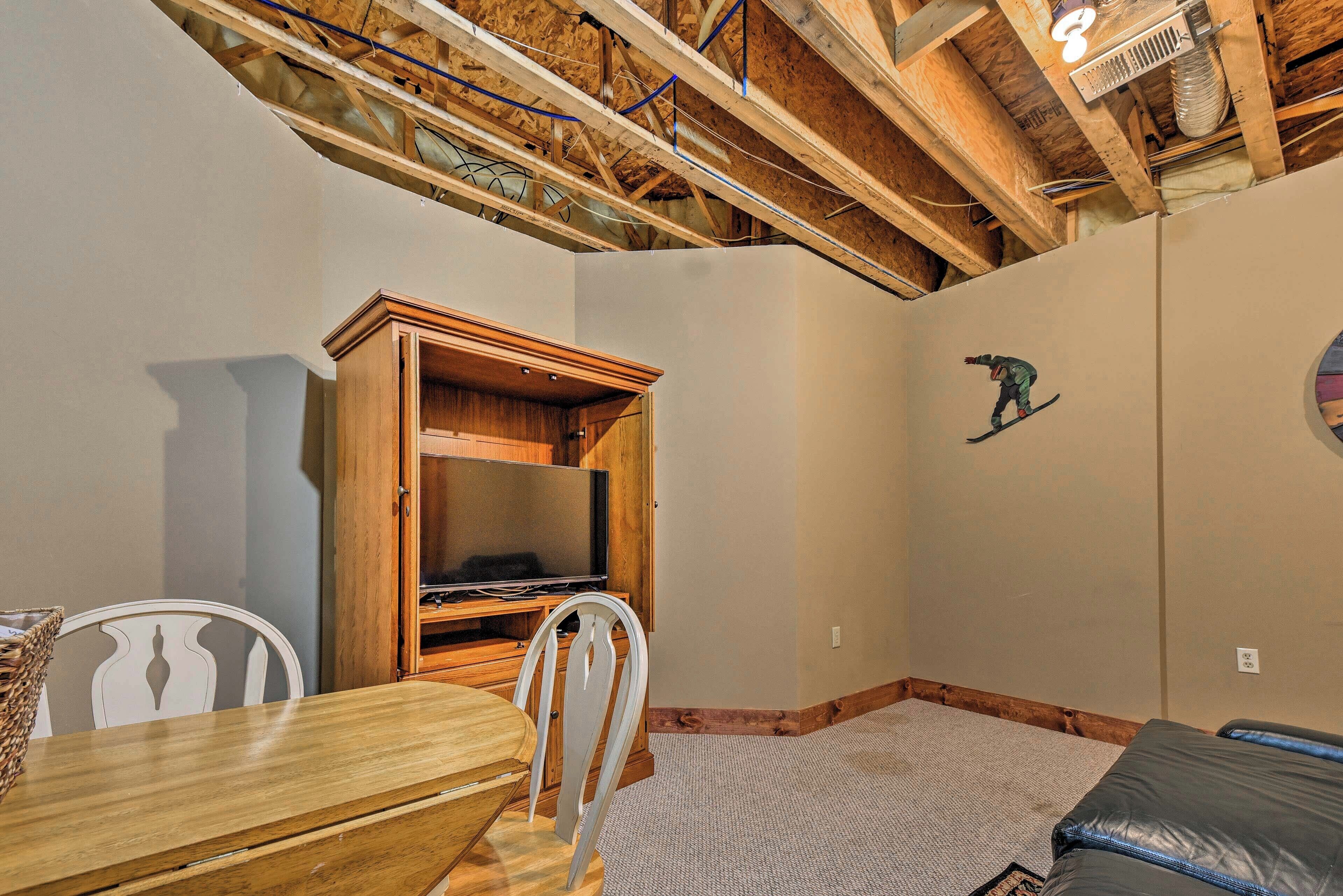 A room with a wooden ceiling, a television in a cabinet, a dining table with chairs, and a carpeted floor.
