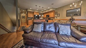 A modern living room with a leather sofa, wooden flooring, and a kitchen in the background.