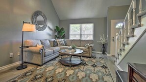A living room with a sectional sofa, a round coffee table, a floor lamp, and a large mirror on the wall. - Modern Townhome w/ Fireplace: Near Stoll Park (Overland Park)