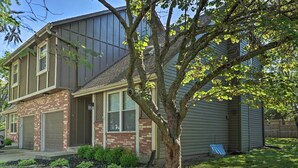A two-story house with a brick facade, a large tree in front, and a garage. - Modern Townhome w/ Fireplace: Near Stoll Park (Overland Park)