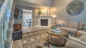 A living room with a stone fireplace, a round mirror, and a sectional sofa. - Modern Townhome w/ Fireplace: Near Stoll Park (Overland Park)