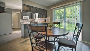 A modern kitchen with dark cabinets, a white refrigerator, and a dining area with a round table and chairs. - Modern Townhome w/ Fireplace: Near Stoll Park (Overland Park)