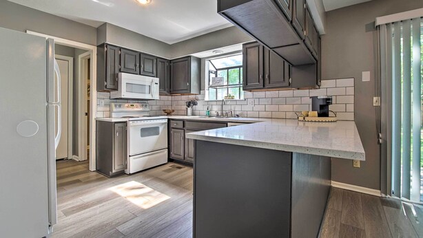 A modern kitchen with dark cabinets, a white refrigerator, a microwave, and a large island with a sink. - Modern Townhome w/ Fireplace: Near Stoll Park (Overland Park)