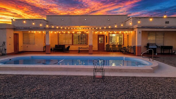 A pool area with string lights, a barbecue grill, and a patio with chairs and tables.