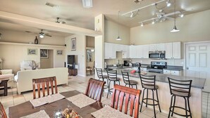 A spacious living area with a dining table, chairs, and a kitchen with white cabinets and appliances.