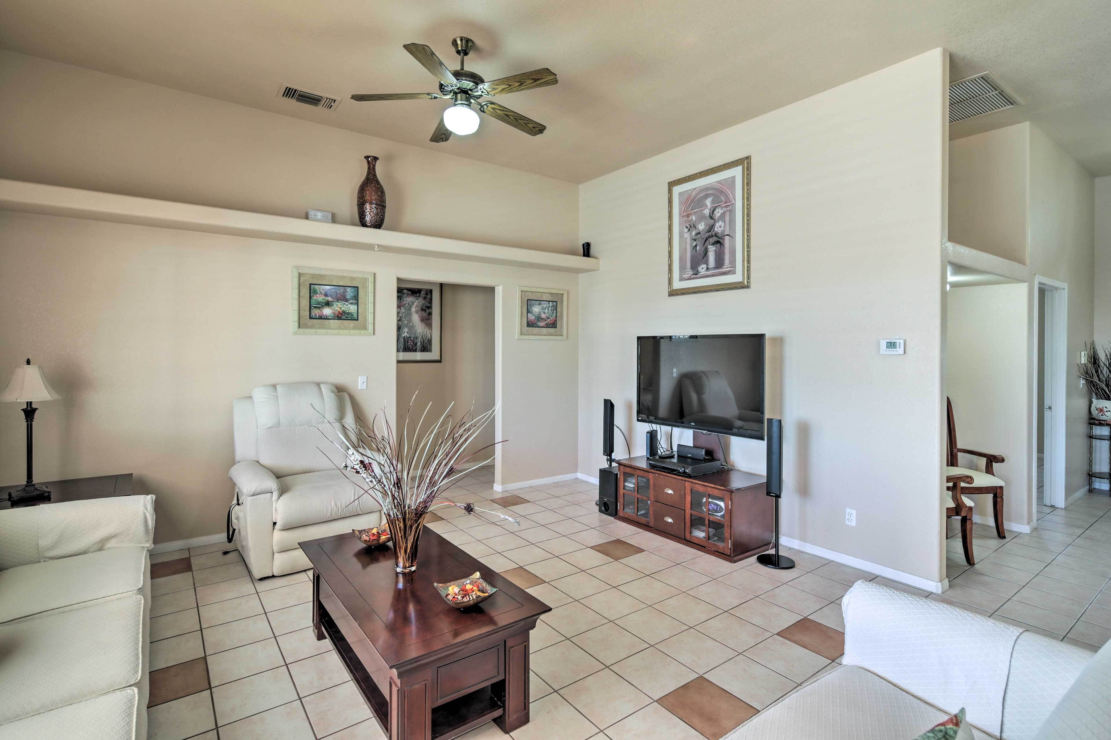 A spacious living room with a ceiling fan, a flat-screen TV, a sofa, a coffee table, and a fireplace.