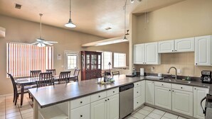 A spacious kitchen with white cabinets, a large island, and a dining area with chairs.