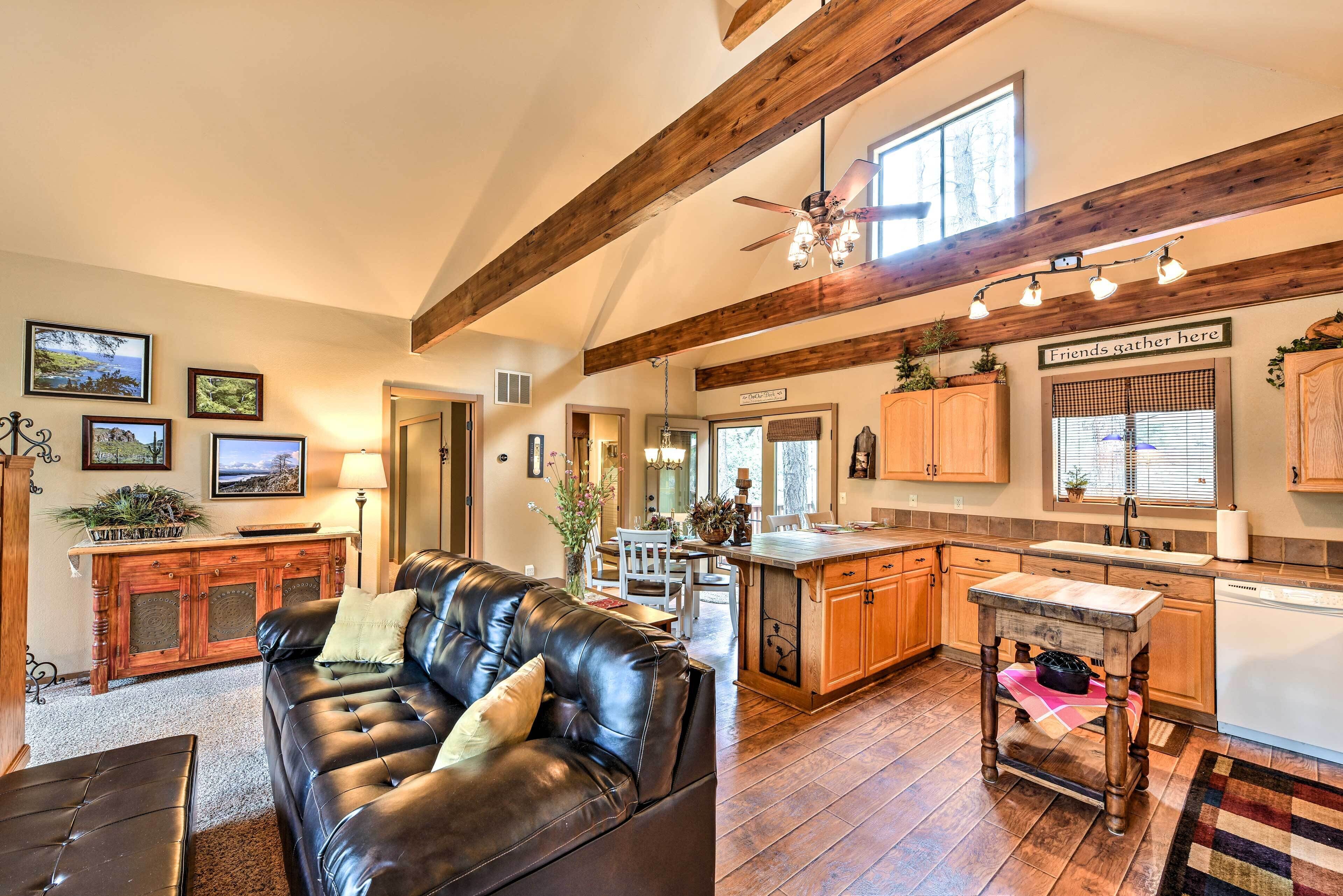 A spacious living room with a leather couch, wooden dining table, and a kitchen area with wooden cabinets and a built-in oven.