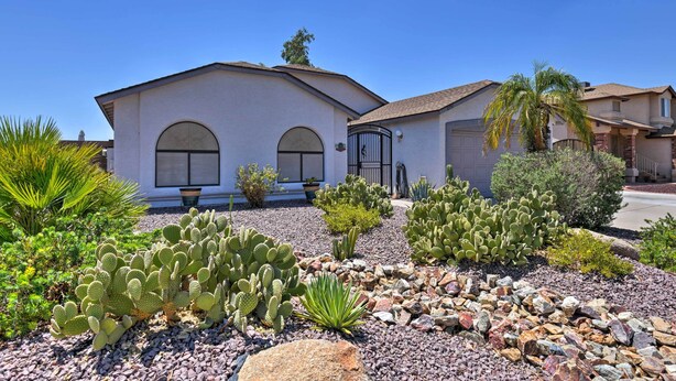 A house with a white exterior, two garage doors, and a well-maintained garden with cacti and other desert plants. - Walk to NFL Games: Glendale Home Near Golf (Glendale)