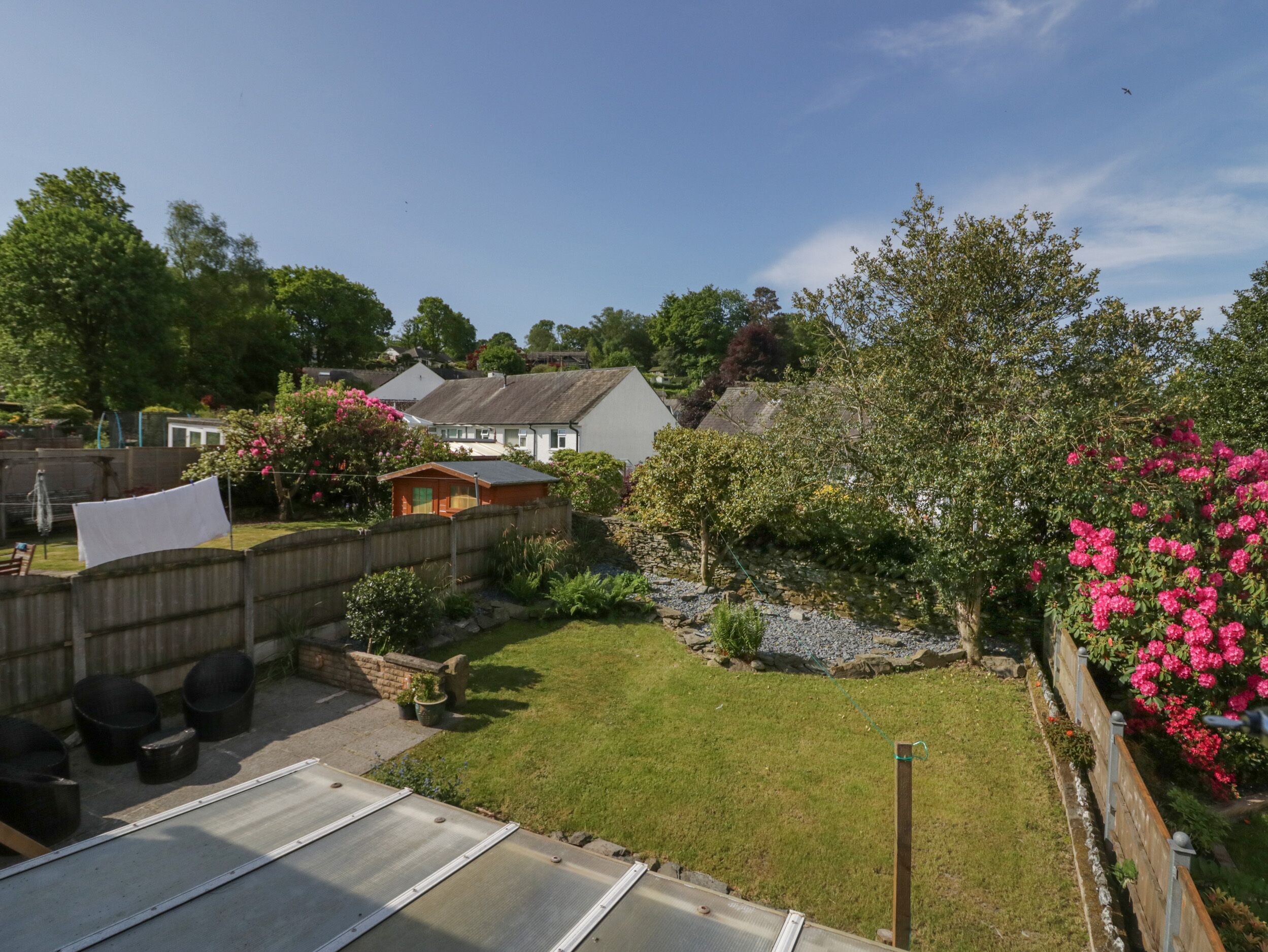 A residential backyard with a wooden fence, a small shed, and a garden with pink flowers.