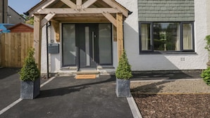 Une maison avec un porche en bois, une porte noire et un petit paillasson.