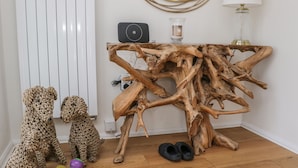 Une pièce comprenant une œuvre d’art en bois, deux chiens, une table avec une lampe et un radiateur.