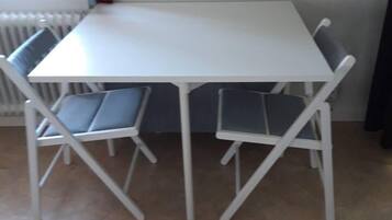 A white table with four chairs, a radiator, and kitchen items on the wall.