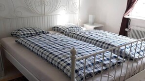 Una cama de metal blanca con cabecera, dos almohadas y una colcha a cuadros.
