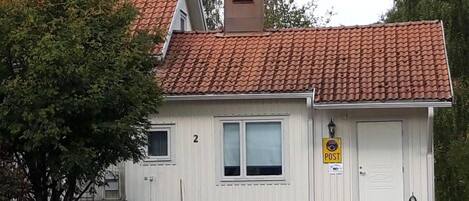 A small, single-story building with a red-tiled roof, a white door, and a small porch area.