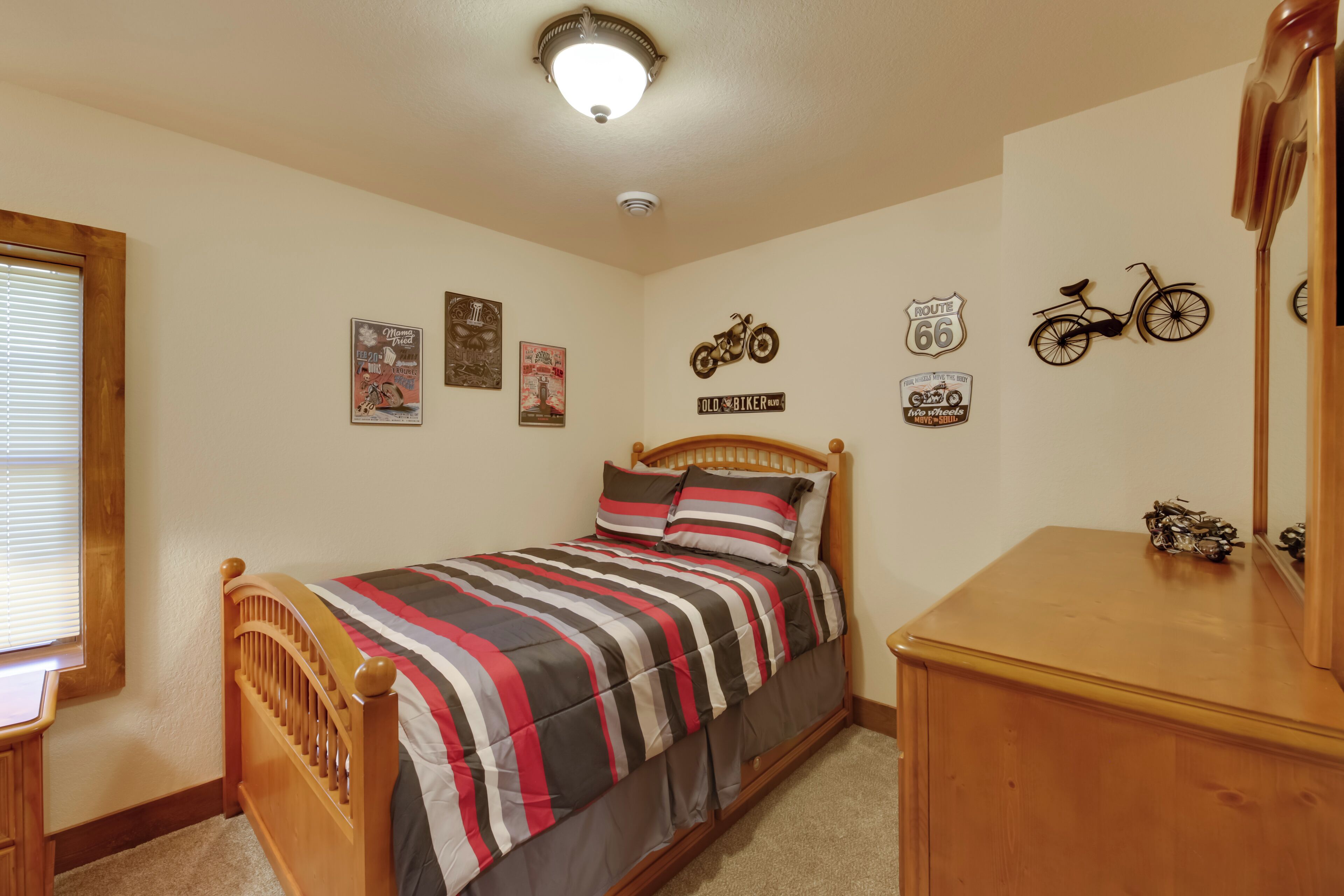 A bedroom with a bed, wooden headboard, and a dresser. There are wall decorations including a motorcycle and Route 66 signs.