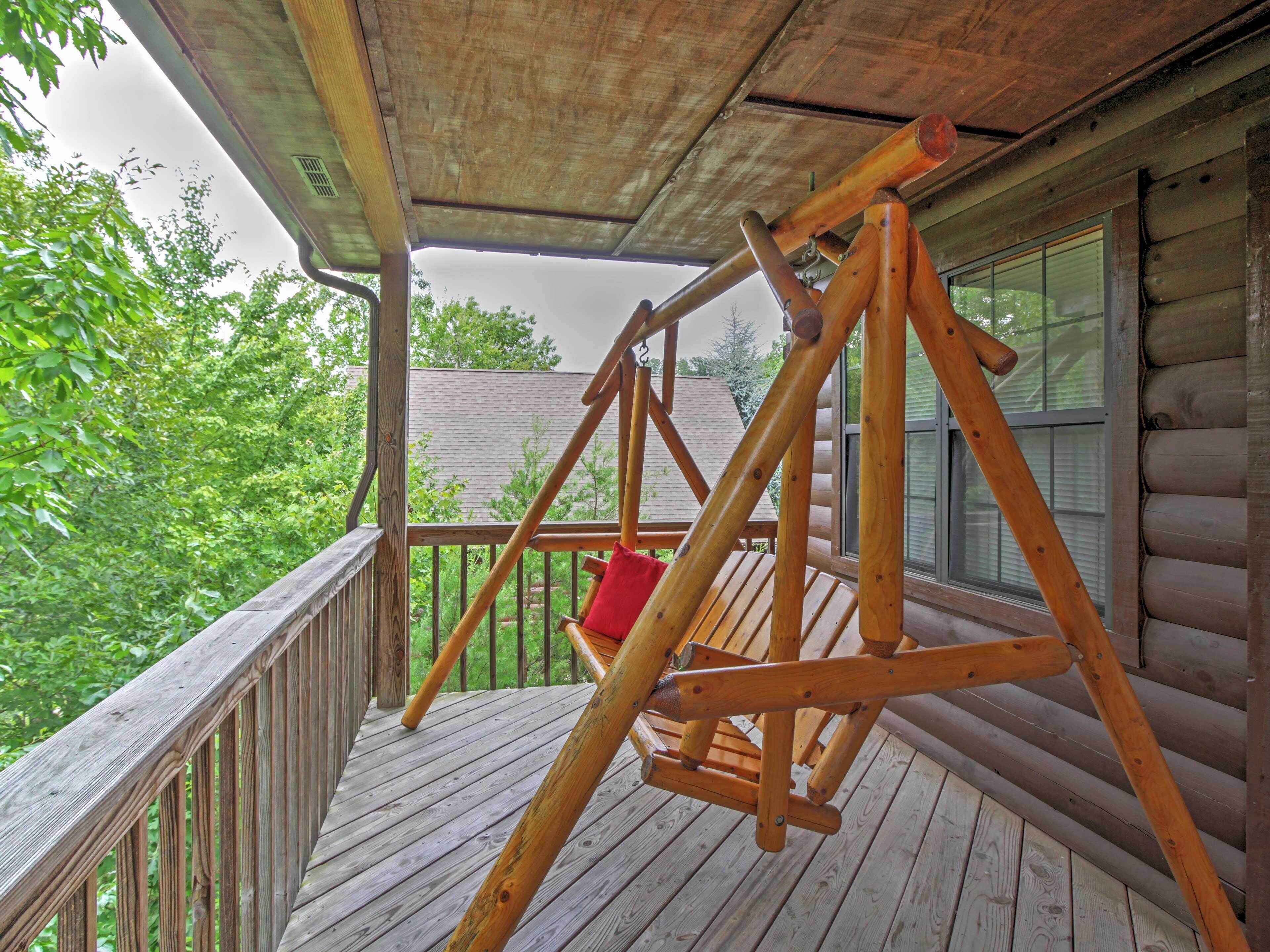 A wooden deck with a swing set, a red cushion, and a window overlooking a green landscape.