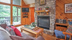 Un salon chaleureux avec une cheminée en pierre, des meubles en bois et une grande fenêtre donnant sur une terrasse.