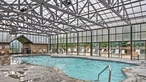 Une piscine intérieure dotée d’un toit en verre, de chaises longues et d’un mur en briques.