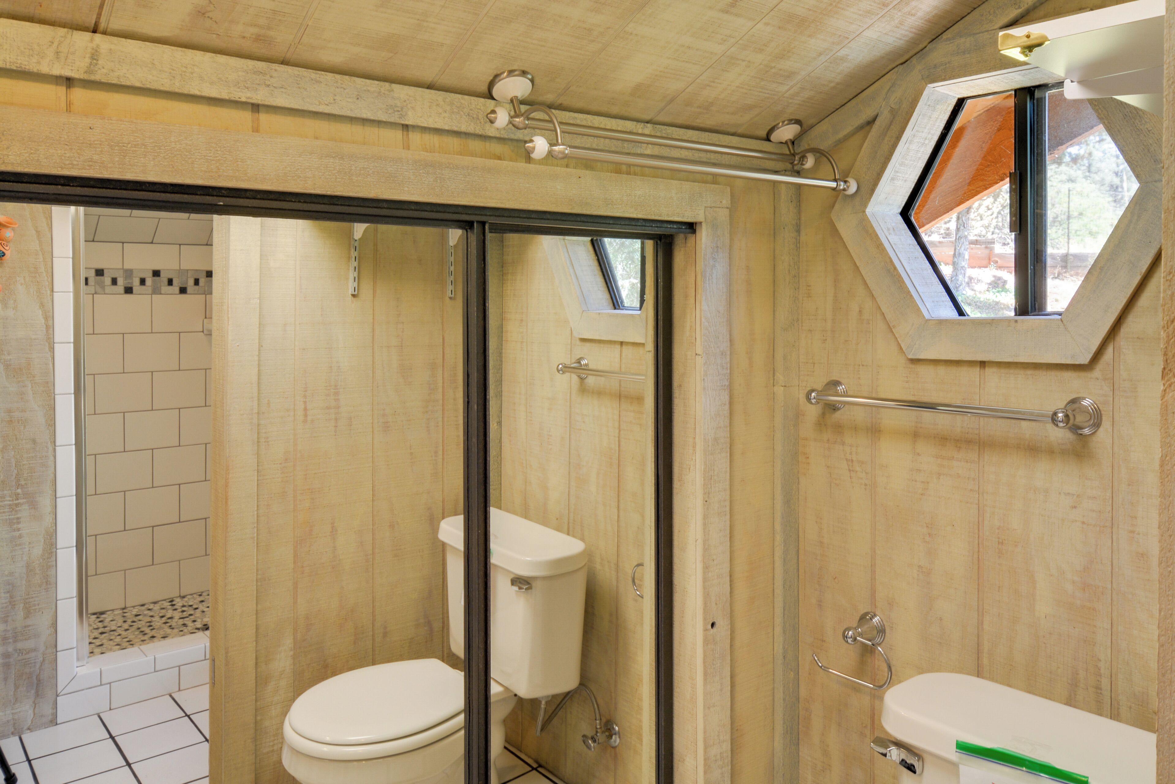 A bathroom with a wooden interior, a shower with a glass door, and a window with a hexagonal frame.