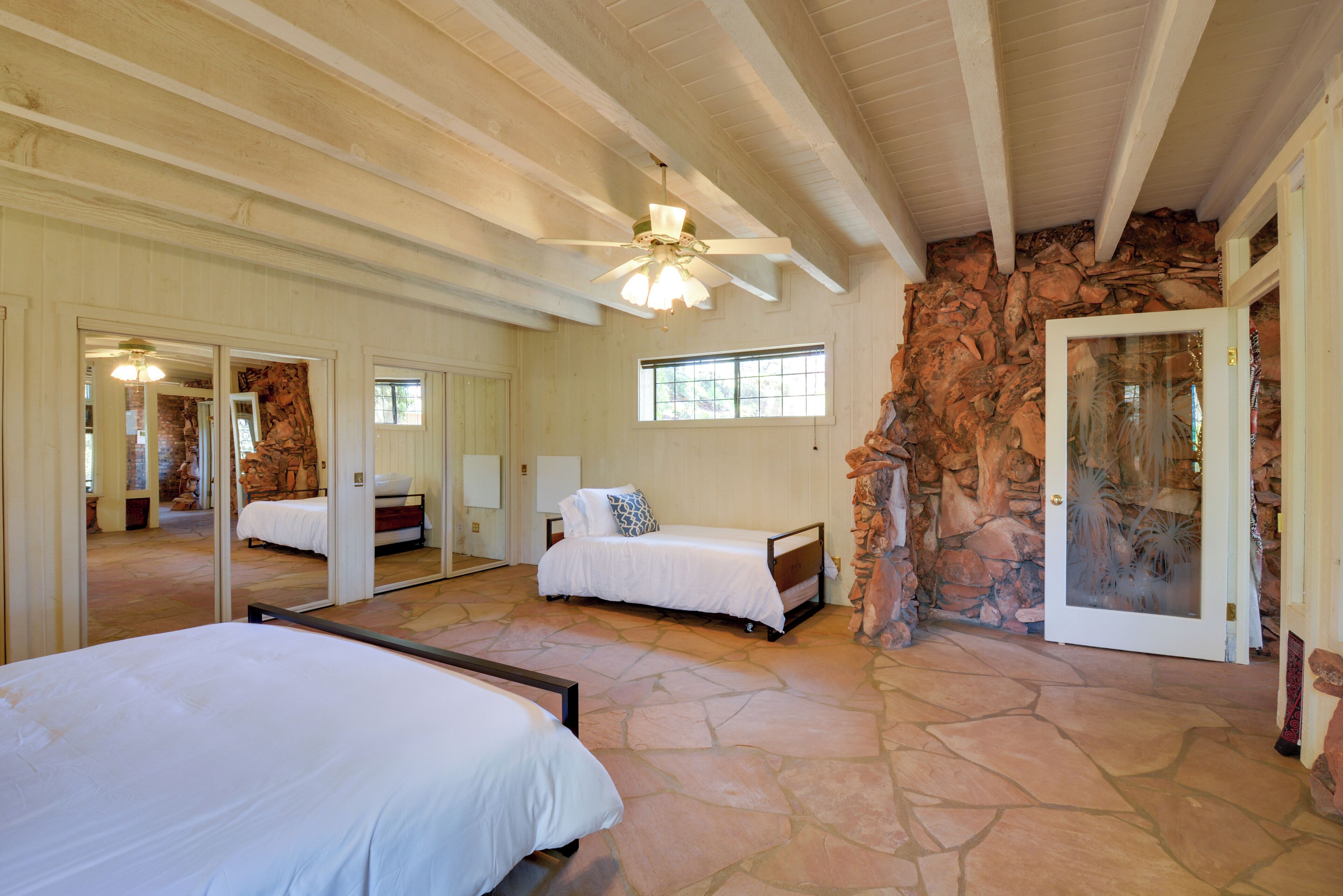 A spacious bedroom with a large bed, a smaller bed, and a stone wall.