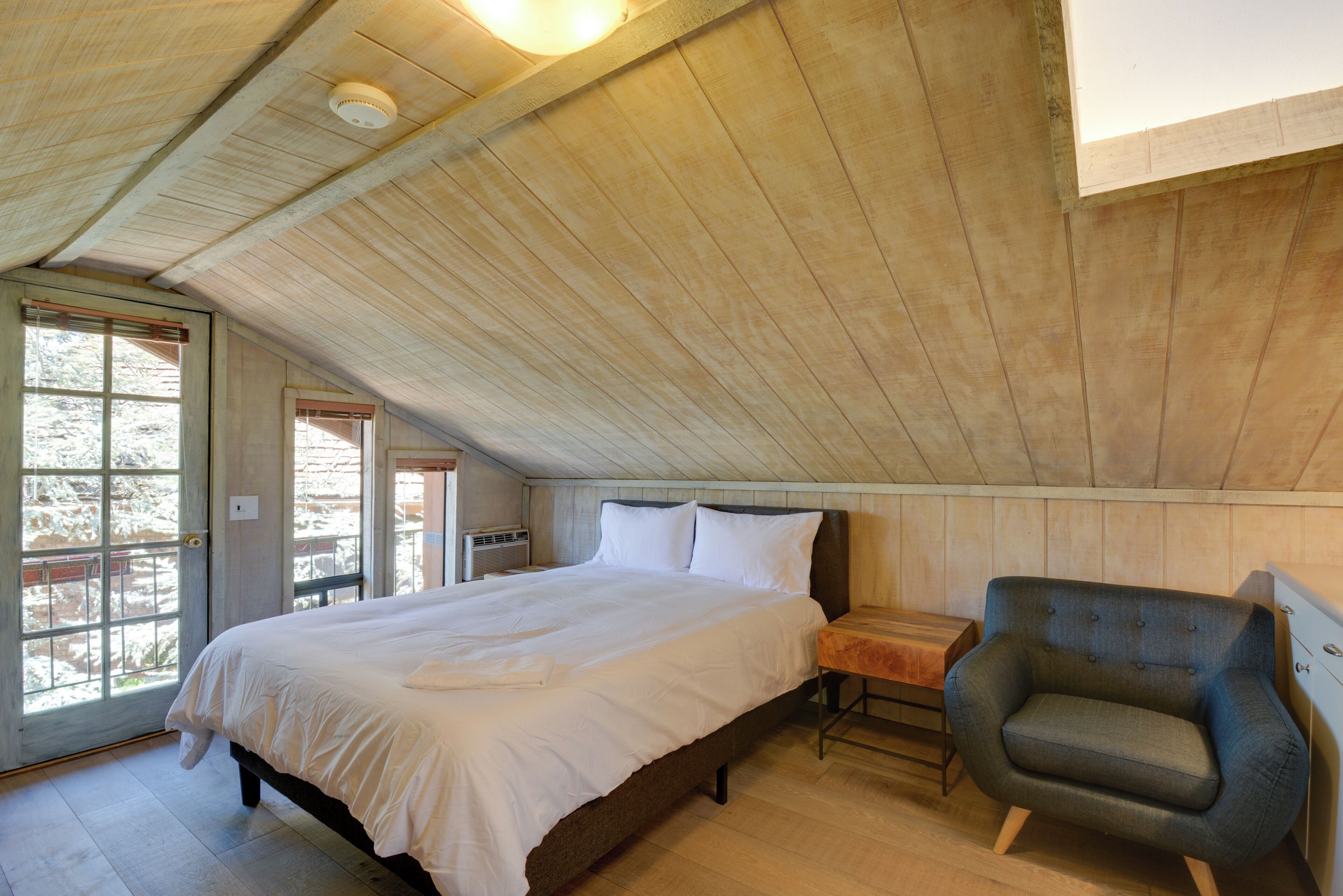 Een slaapkamer met een houten plafond, een bed met witte lakens, een stoel en een kleine tafel.