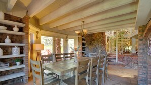 Un comedor rústico con una mesa y sillas de madera, rodeado de estantes con objetos decorativos y una pared de piedra.