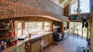 Una cocina con pared de ladrillo, ventanas amplias, estufa y comedor con sillas y mesa.