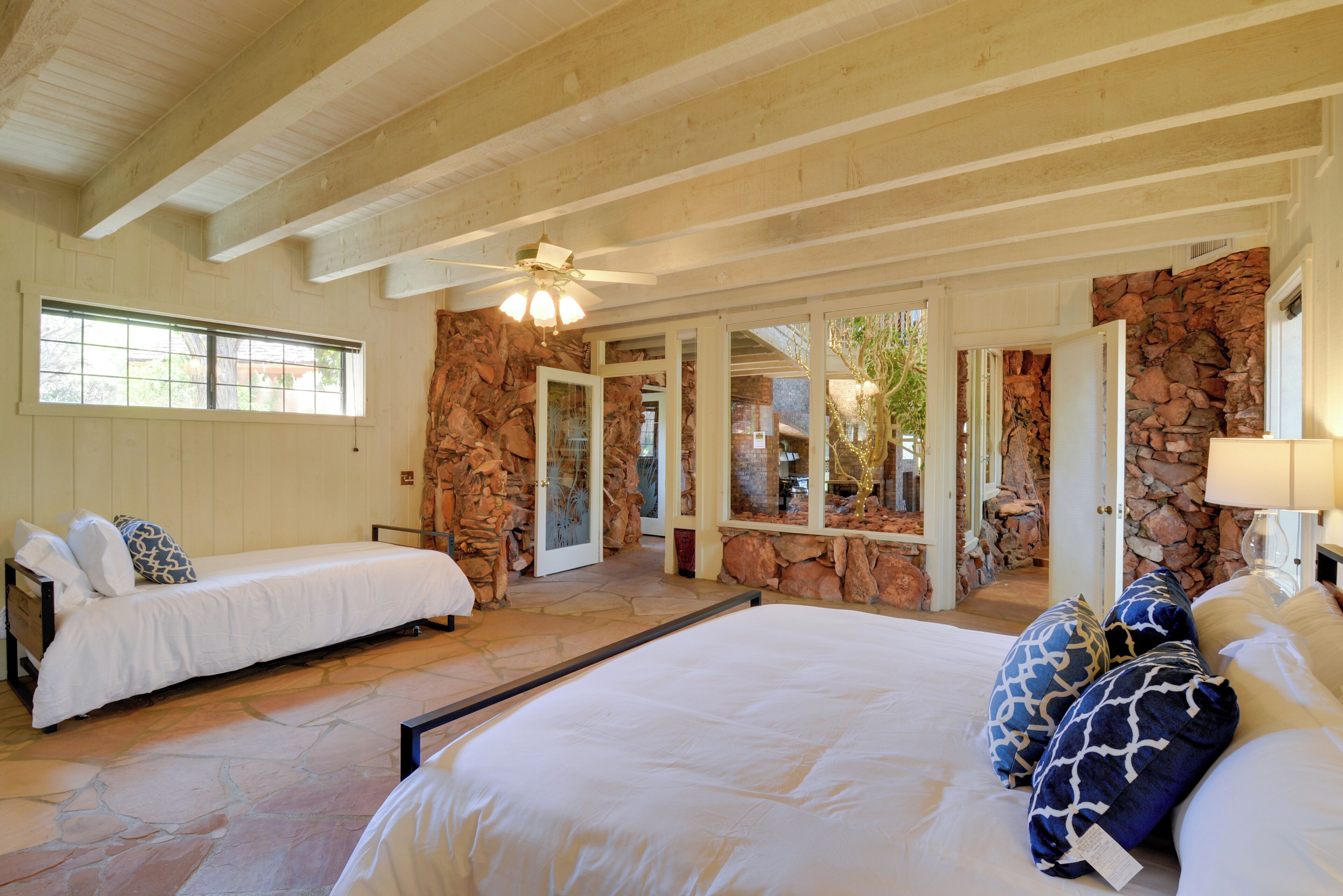 Un dormitorio con dos camas individuales, una cama grande, paredes de piedra, vigas de madera y un ventilador de techo.