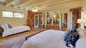 A bedroom with two single beds, a large bed, stone walls, wooden beams, and a ceiling fan. - Stone Manor Hot Tub Red Rock Views Guest Suite (Sedona)