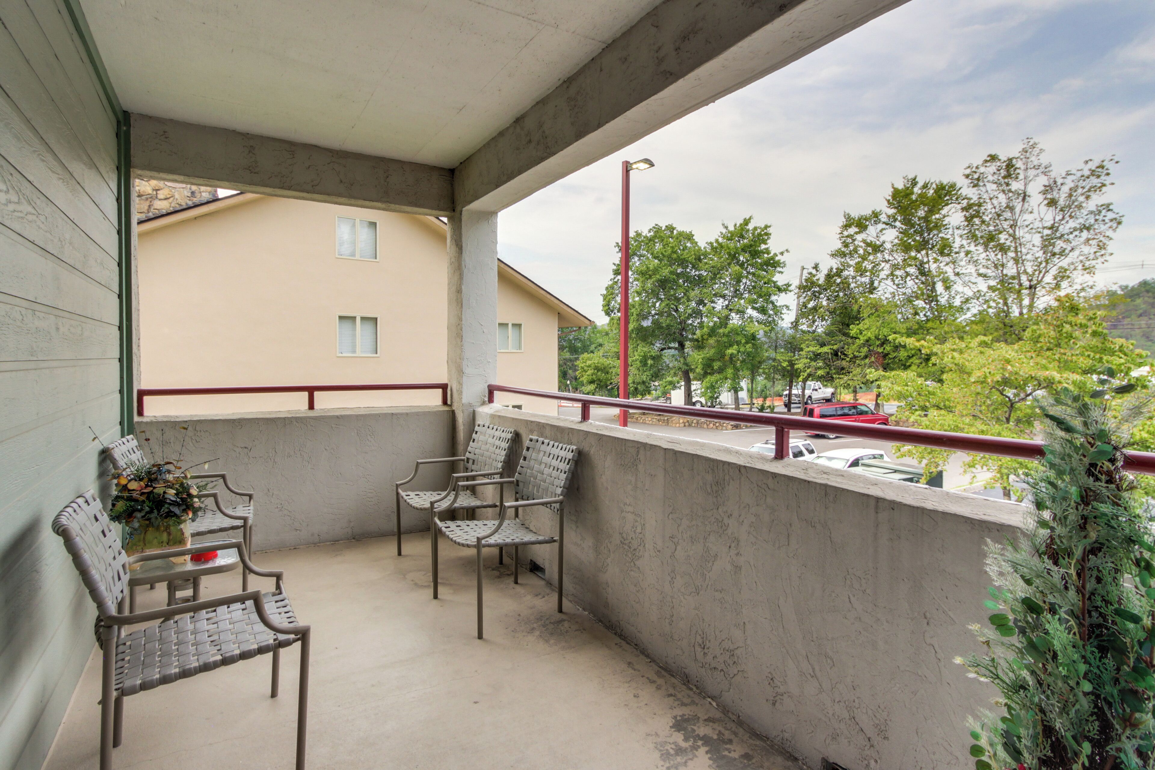 Un balcón con dos sillas y una mesa, con vista a una calle con coches y árboles.