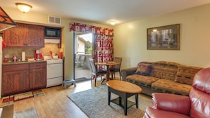 Un espacio habitable compacto con kitchenette, un sofá, una mesa de comedor y una butaca de cuero rojo.