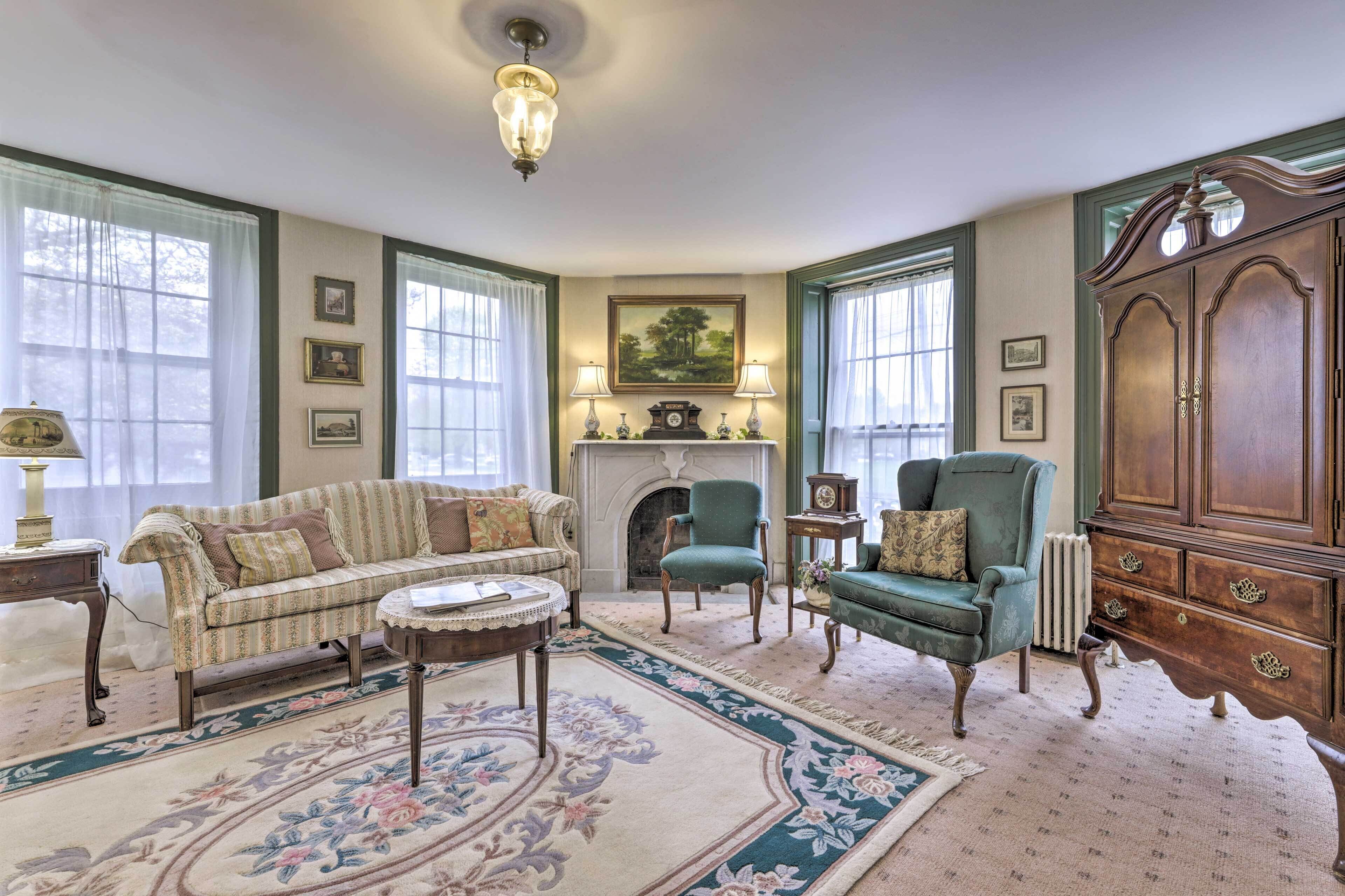 Een klassieke woonkamer met een bank, fauteuils, een open haard en een grote houten kast.