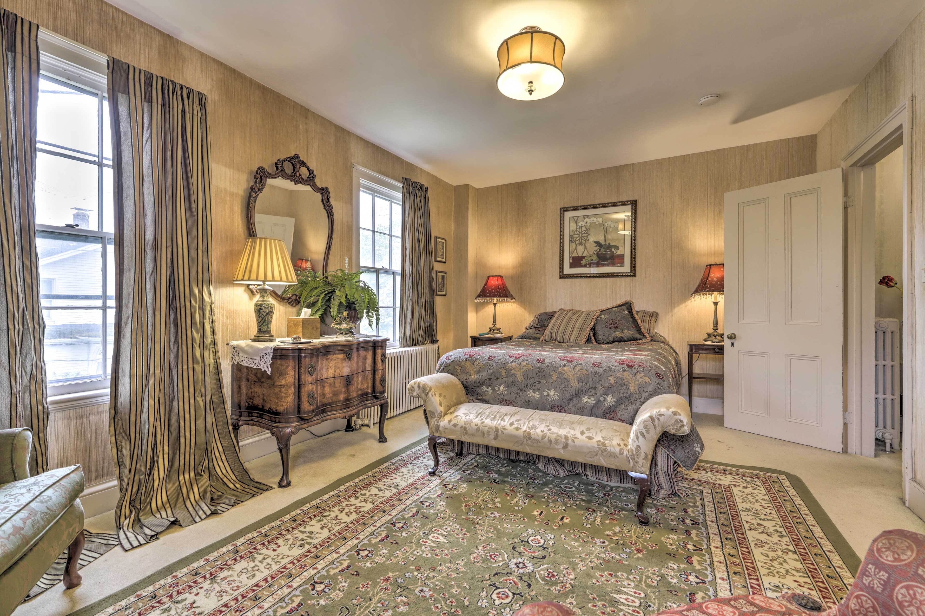 A traditional bedroom with a large bed, a bench, a dresser, and a mirror.