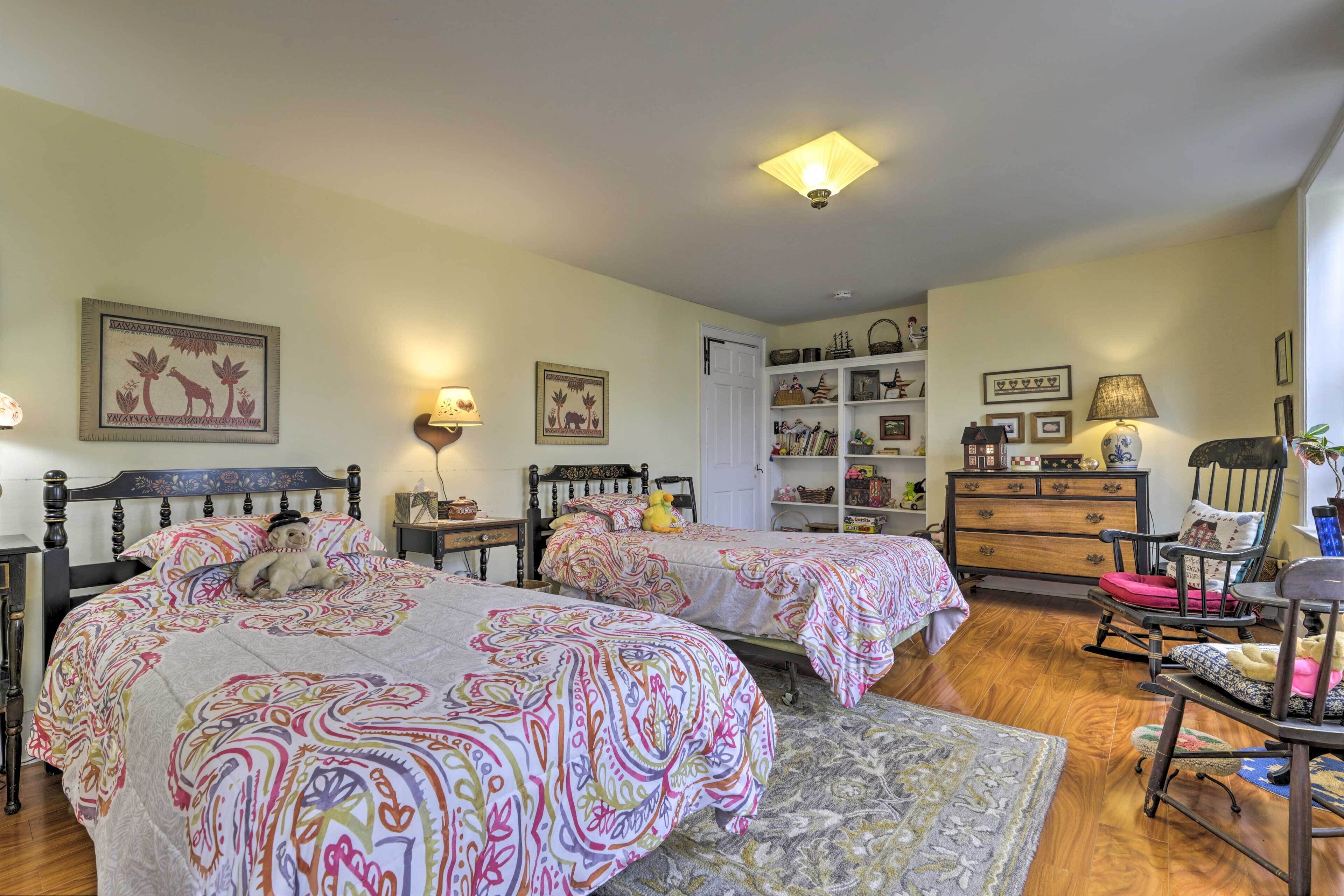 Um quarto aconchegante com duas camas, um aparador de madeira, uma cadeira de balanço e uma estante de livros.