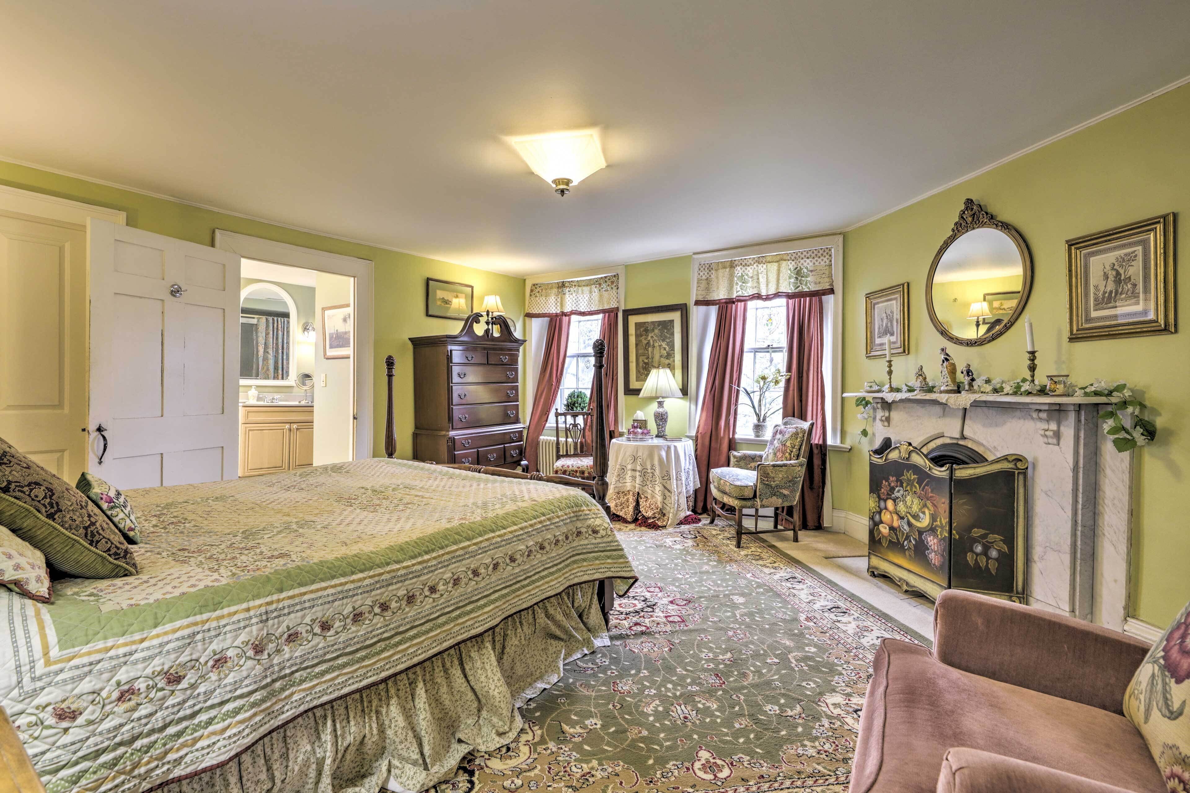 A bedroom with a large bed, a dresser, a chair, a table, and a fireplace.