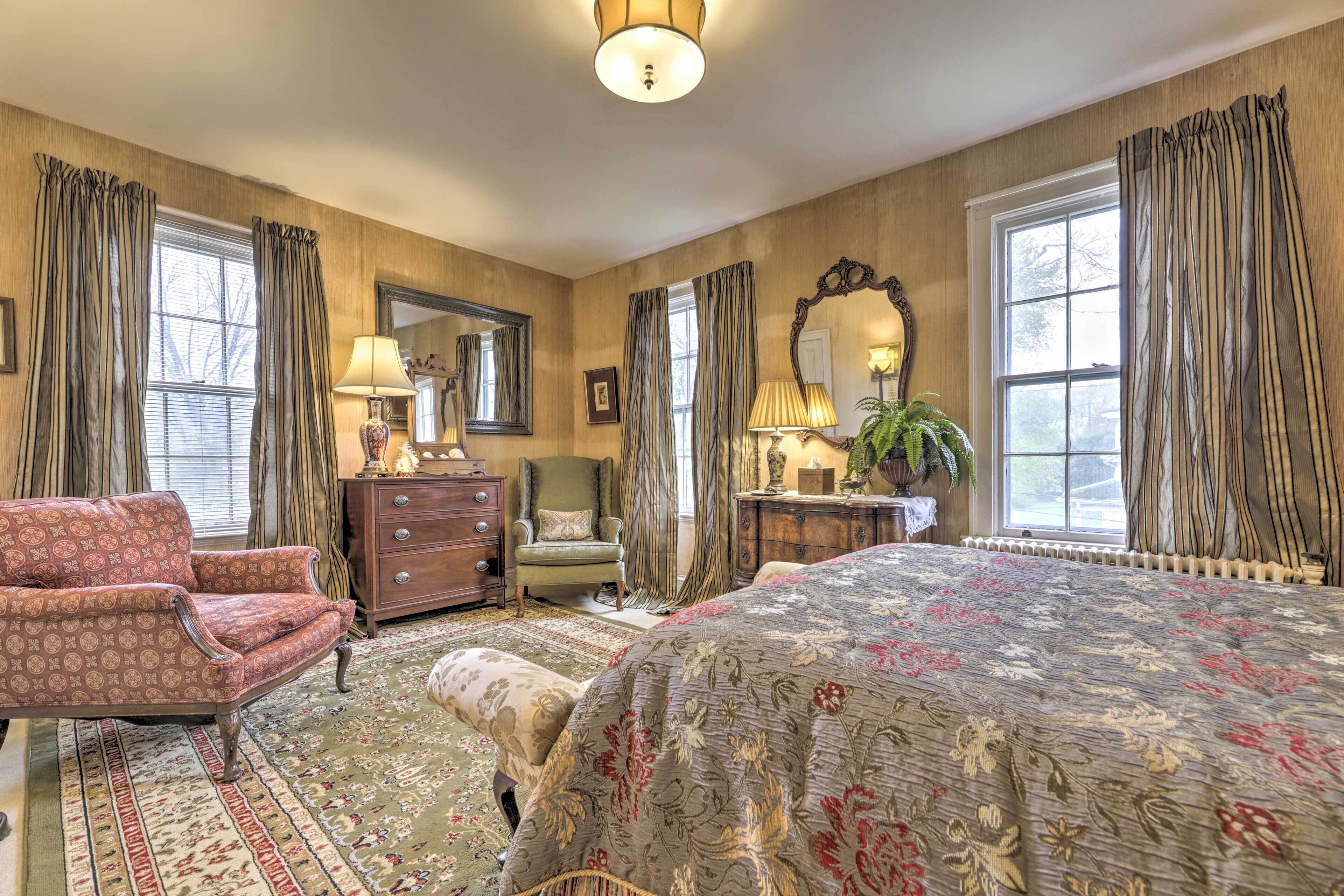 Een klassieke slaapkamer met een groot bed, een stoel, een dressoir en een spiegel.
