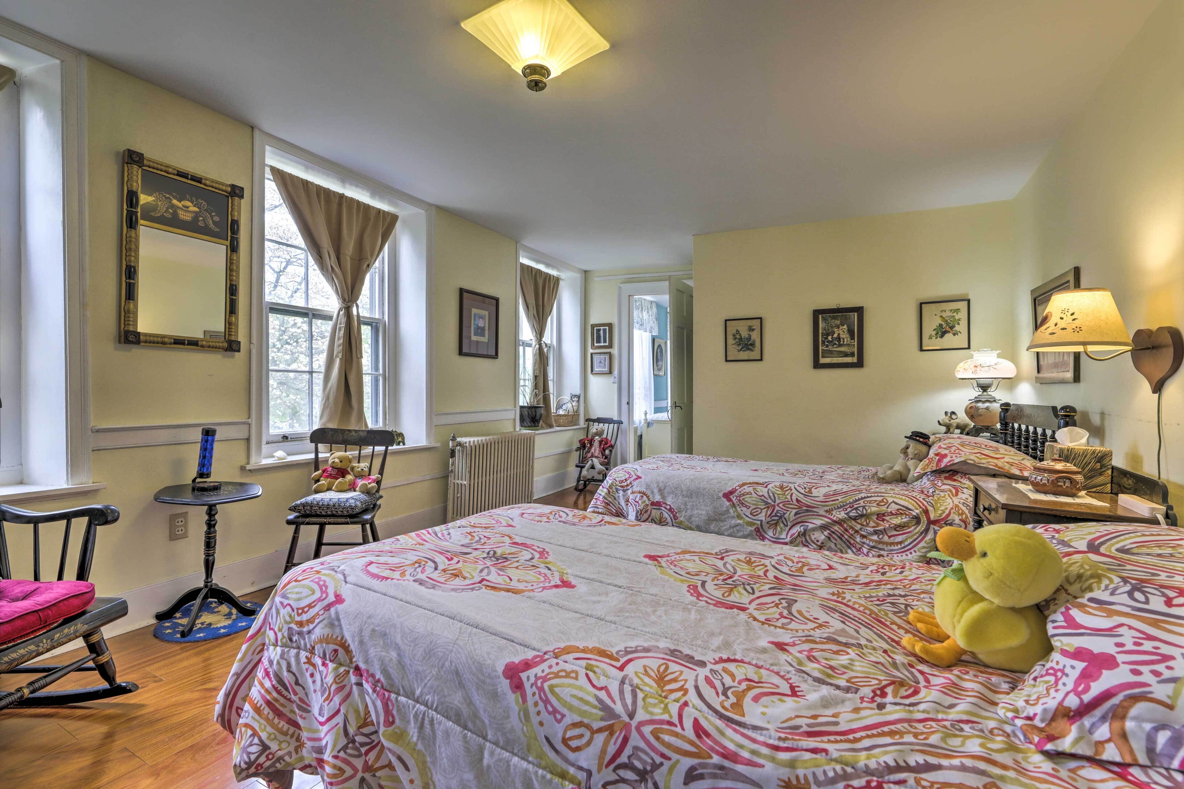 A room with two beds, a rocking chair, a small table, and a window with curtains.