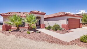 A two-story house with a red-tiled roof, a garage, and a landscaped front yard with desert plants.